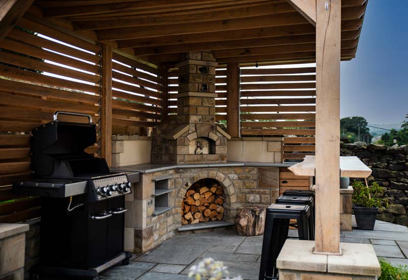 A large patio area of a garden containing a pizza oven, barbecue area and pizza oven.